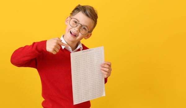 Un bambino sorridente indica un foglio che mostra una valutazione scolastica.