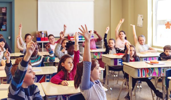 Una classe che risponde a una domanda del professore. Gli studenti alzano tutti la mano.
